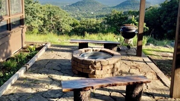 An outdoor seating area with a stone fire pit, a bench, and a pergola overlooking a mountainous landscape. - Beautiful Mountain Vacation Rental (Pipe Creek)