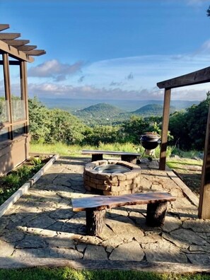 An outdoor seating area with a stone fire pit, a bench, and a pergola overlooking a mountainous landscape. - Beautiful Mountain Vacation Rental (Pipe Creek)