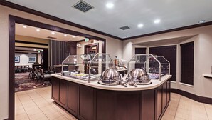 Een ontbijtbuffet met afgedekte etalages, een zithoek met tafels en stoelen, en een uitzicht op het interieur van het hotel.