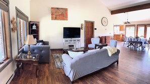 A spacious living room with a large sofa, a TV, and a dining area with a table and chairs. - Ranch-style home with horse property and fenced yard (Frenchtown)