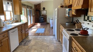 A kitchen with wooden cabinets, a stove, a refrigerator, and a brick fireplace. - Ranch-style home with horse property and fenced yard (Frenchtown)