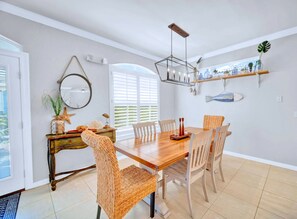 Un coin repas avec une table en bois, des chaises en osier, un lustre et une étagère murale agrémentée d’objets décoratifs.