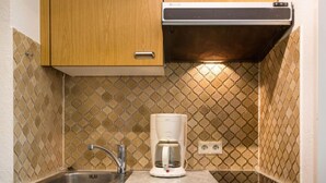 Una cocina compacta con un lavamanos, una cafetera y armarios de madera.