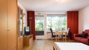Habitación de hotel con cama, escritorio y silla, televisión, armario y ventana con cortinas.