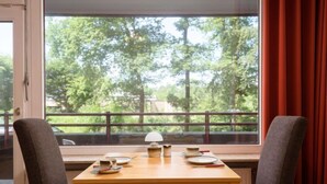 Un comedor con una mesa preparada para dos, una ventana con vista a árboles y una cortina roja.