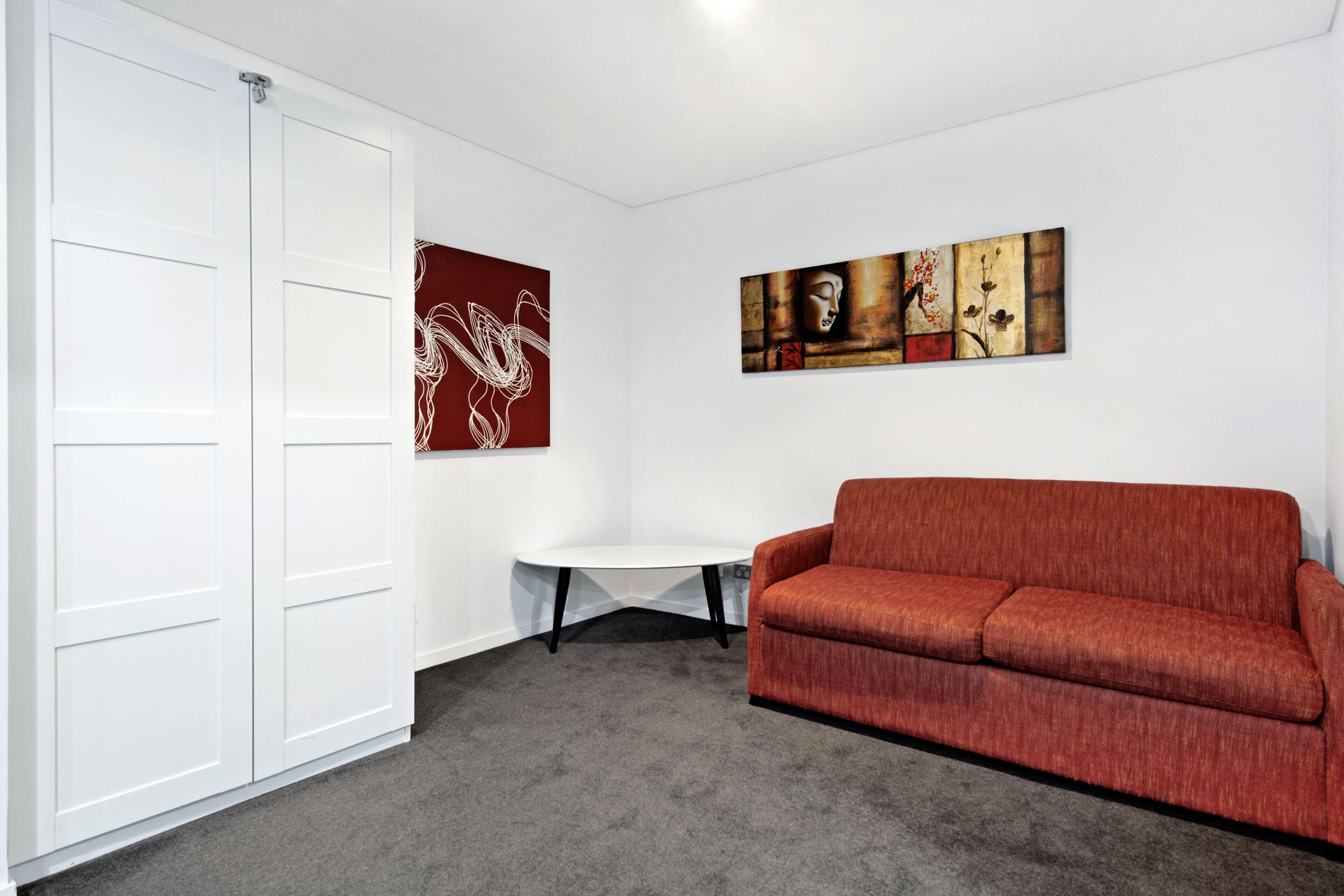 A room with a red sofa, a white table, and two artworks on the wall.