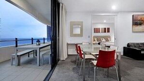 A modern hotel room with a balcony, a dining area with a table and chairs, a sofa, and a painting on the wall. - Wave Apartments Broadbeach (Broadbeach)