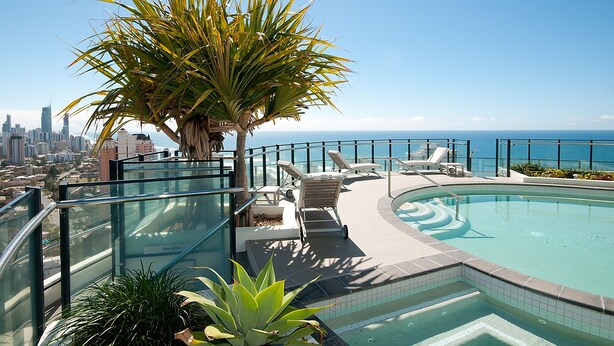 A rooftop pool with lounge chairs, a palm tree, and a city skyline view. - Wave Apartments Broadbeach (Broadbeach)