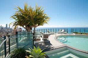 Una piscina en la azotea con sillones de descanso, una palmera y vistas al horizonte de la ciudad.