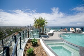 A rooftop pool with a glass balustrade, lounge chairs, and a palm tree. - Wave Apartments Broadbeach (Broadbeach)