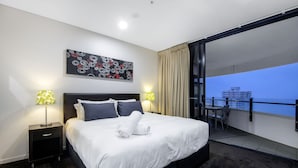A modern hotel room with a large bed, two bedside tables with lamps, a view of the cityscape through a balcony. - Wave Apartments Broadbeach (Broadbeach)