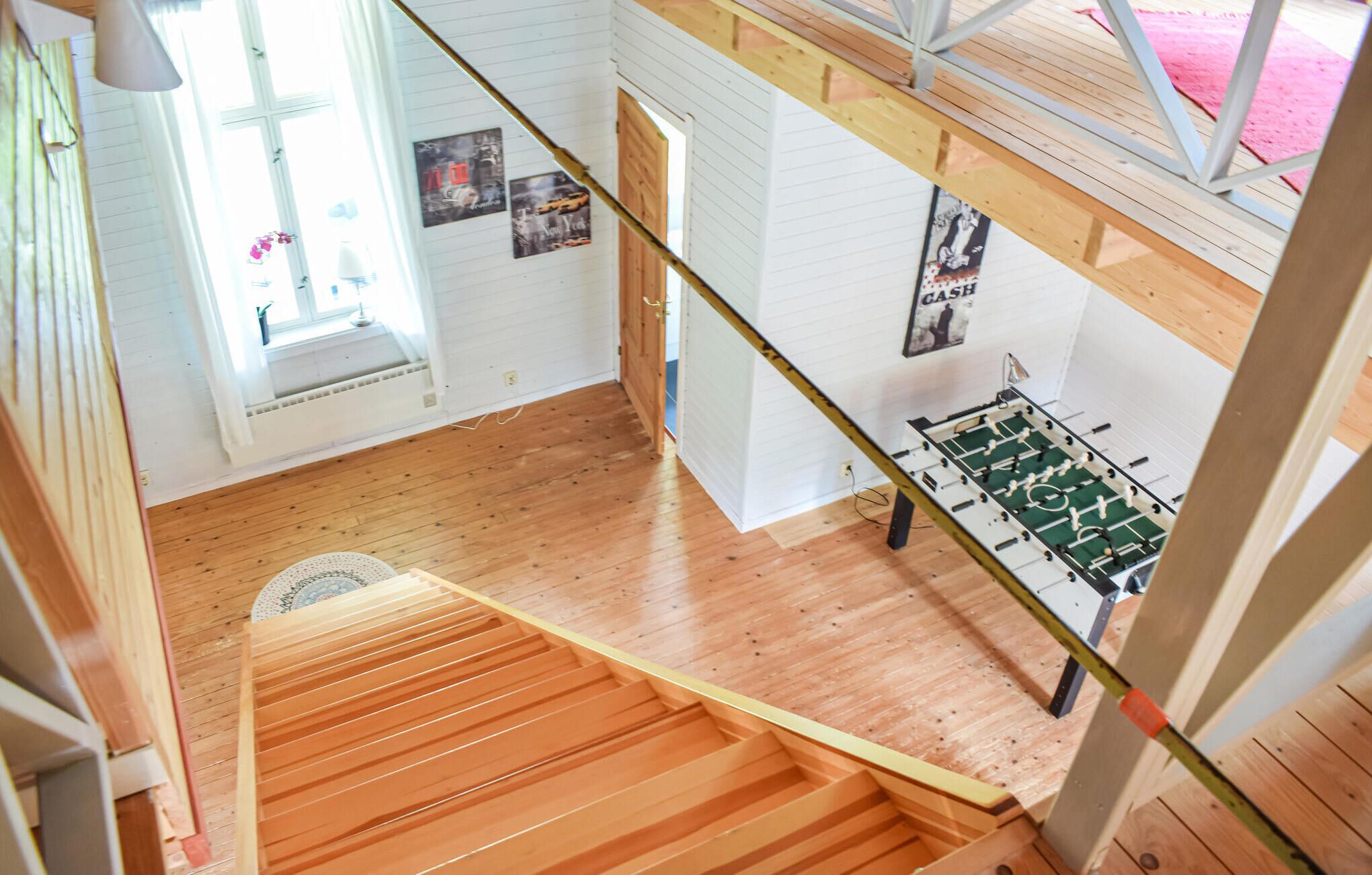 A room with wooden flooring, a foosball table, and a window with curtains.