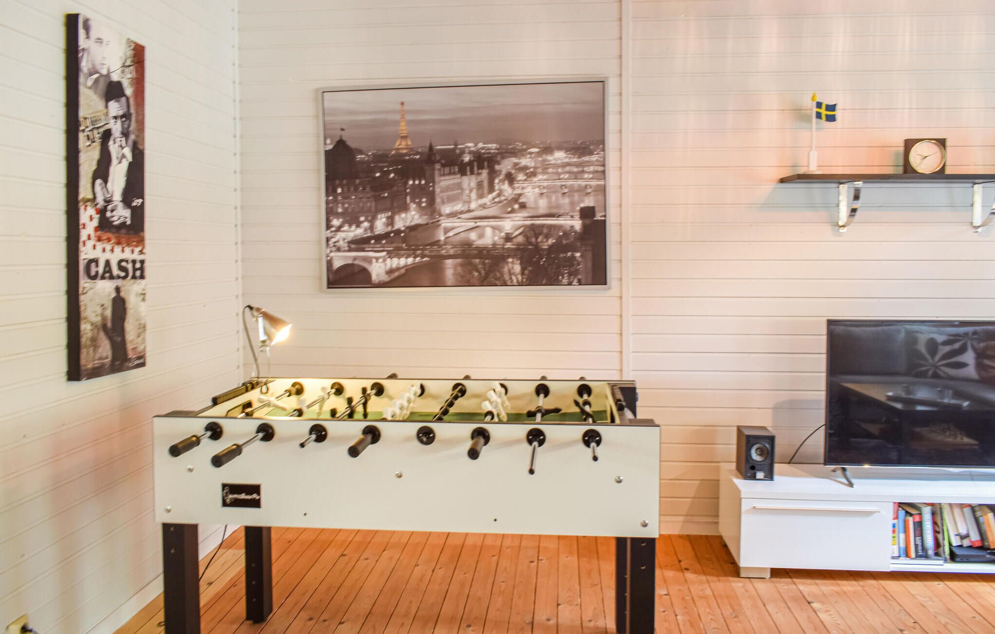 A room with a foosball table, a mounted television, and a poster of a cityscape.