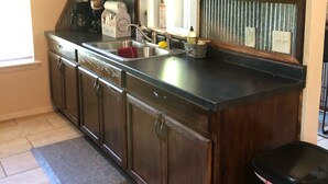 A kitchen with wooden cabinets, a stainless steel sink, and a black trash can.