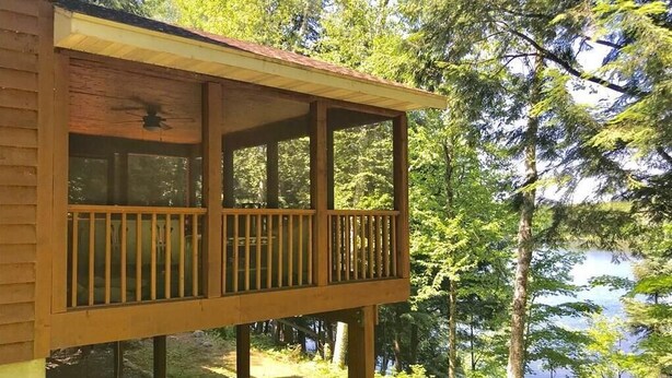 A wooden deck with a railing, overlooking a lake surrounded by trees. - Amazing Fall Colors, Nature, Fireplaces, Screened Porch, Secluded! (Hayward)