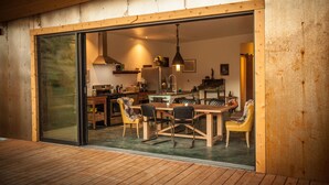 Une cuisine moderne dotée d’une grande table à manger et de chaises, d’un plafond en bois et d’une porte-fenêtre coulissante donnant sur un espace extérieur.