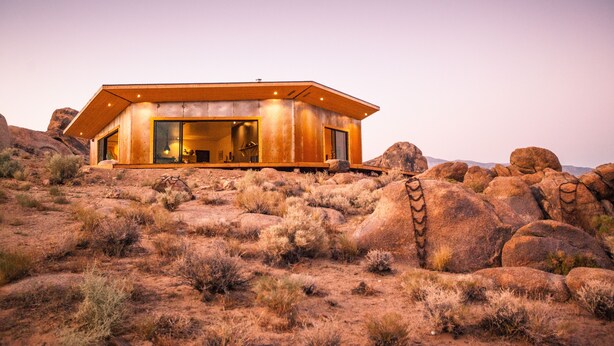 Un bâtiment moderne doté d’un toit plat, de grandes fenêtres et d’une façade en pierre, situé dans un paysage rocheux et aride.
