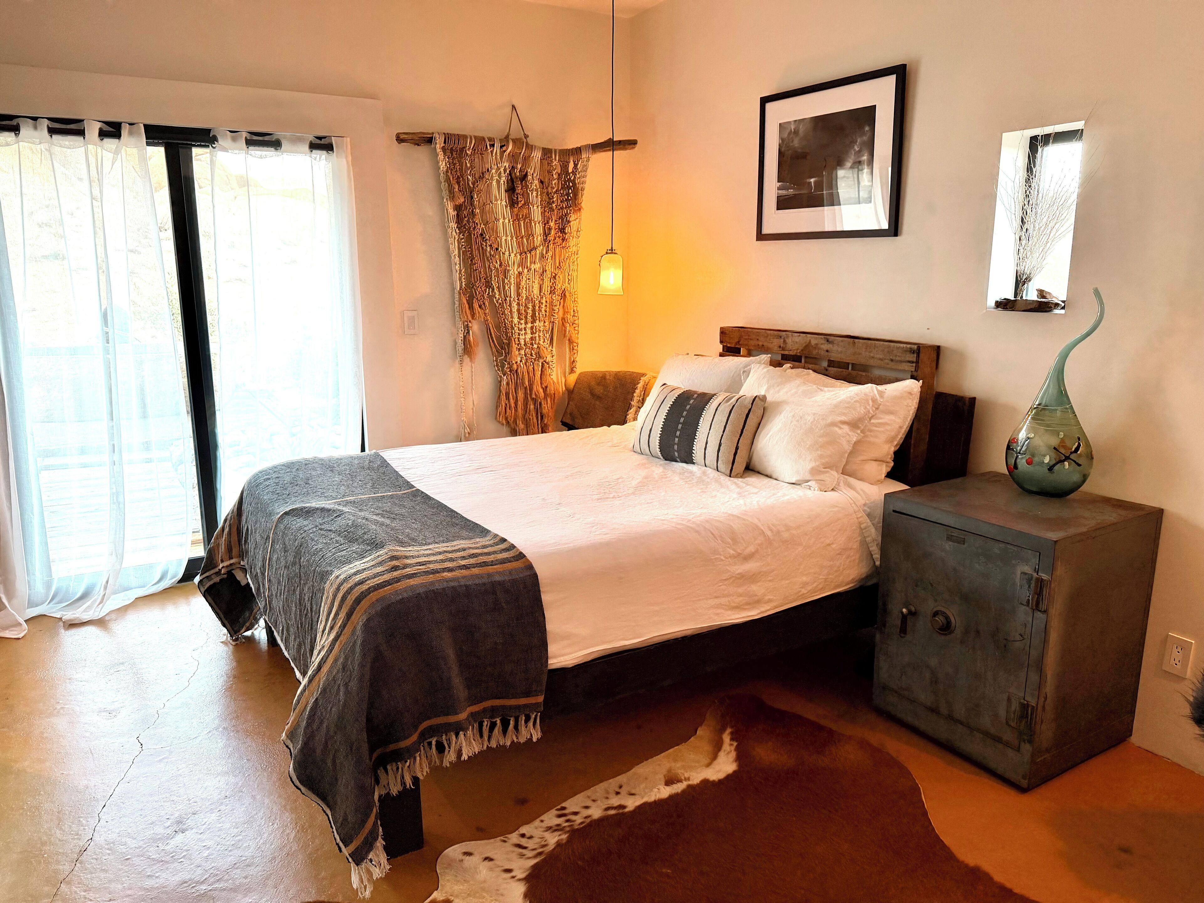 A bedroom with a bed, a nightstand, a lamp, and a wall-mounted picture.