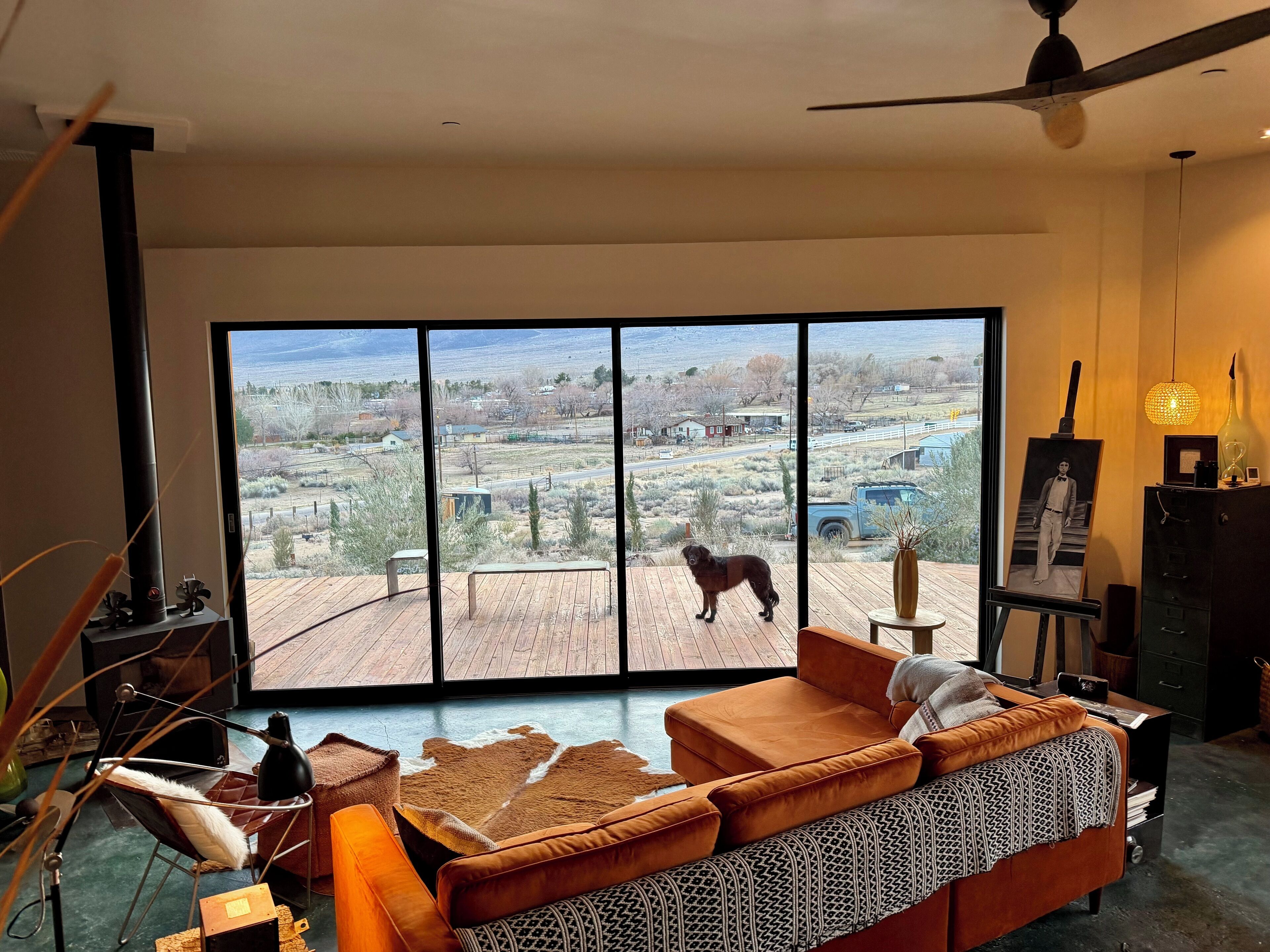 A spacious living room with a large sliding glass door leading to an outdoor deck. The room features a modern sofa, a small table, and a ceiling fan.