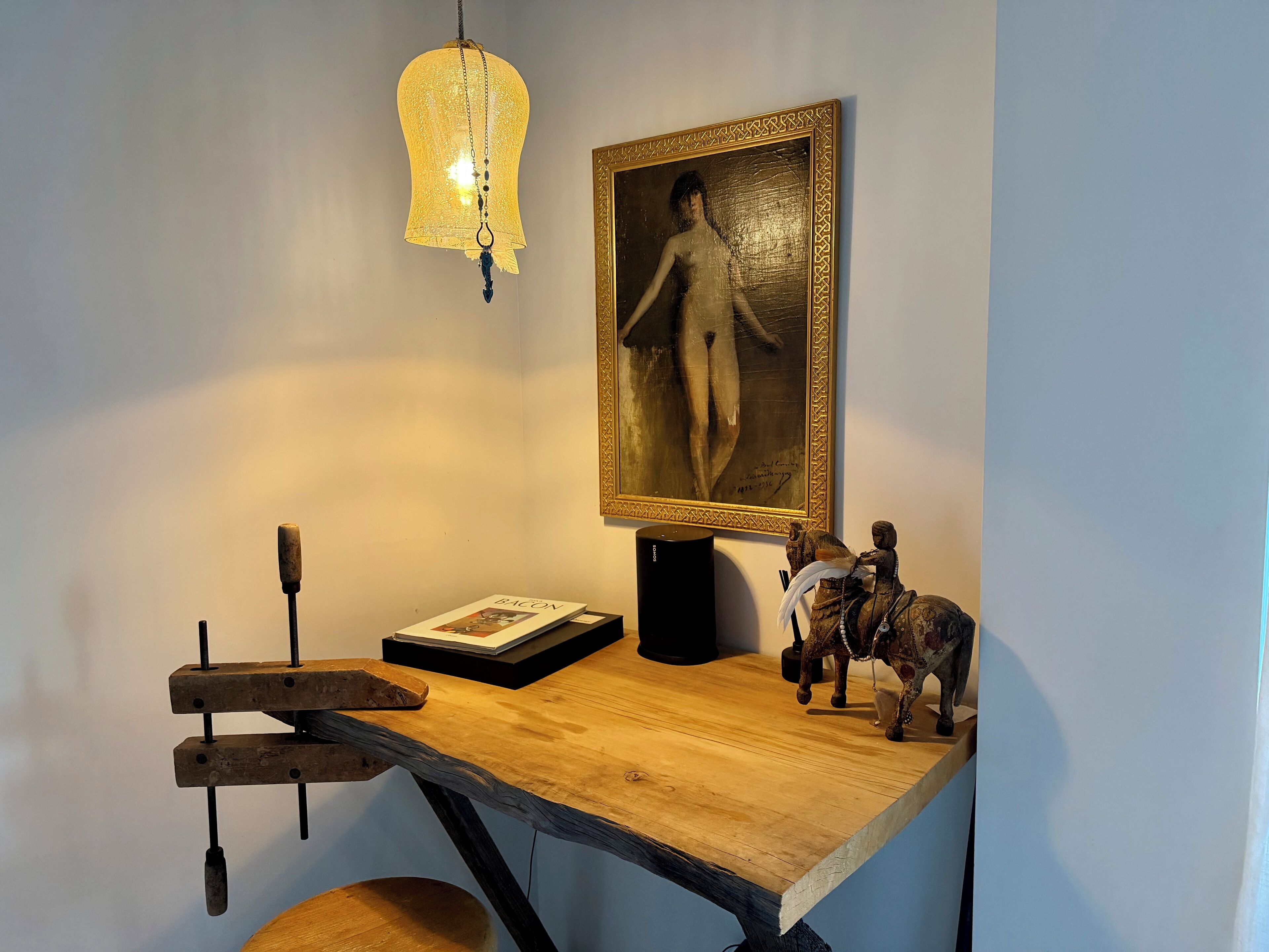 Un bureau en bois orné d’un tableau encadré, d’une statuette de cheval décorative et d’un luminaire suspendu.