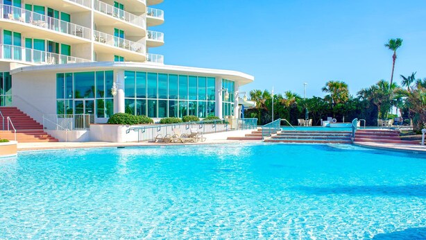 A large swimming pool with a modern building featuring balconies and large windows in the background.