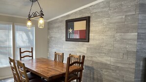 A dining area with a wooden table and chairs, a hanging light fixture, and a framed picture on the wall.