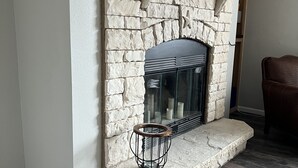 A stone fireplace with a flat-screen TV mounted above it, a small side table, and a brown leather chair in a room with wooden flooring.