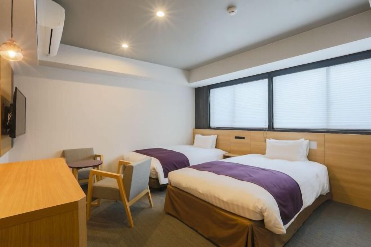 Una habitación de hotel con dos camas, un escritorio, una silla y una televisión.