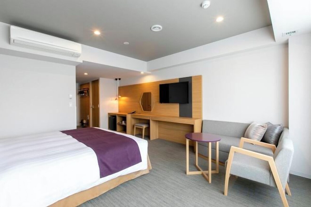 A hotel room with a bed, a desk, a chair, a sofa, and a TV.