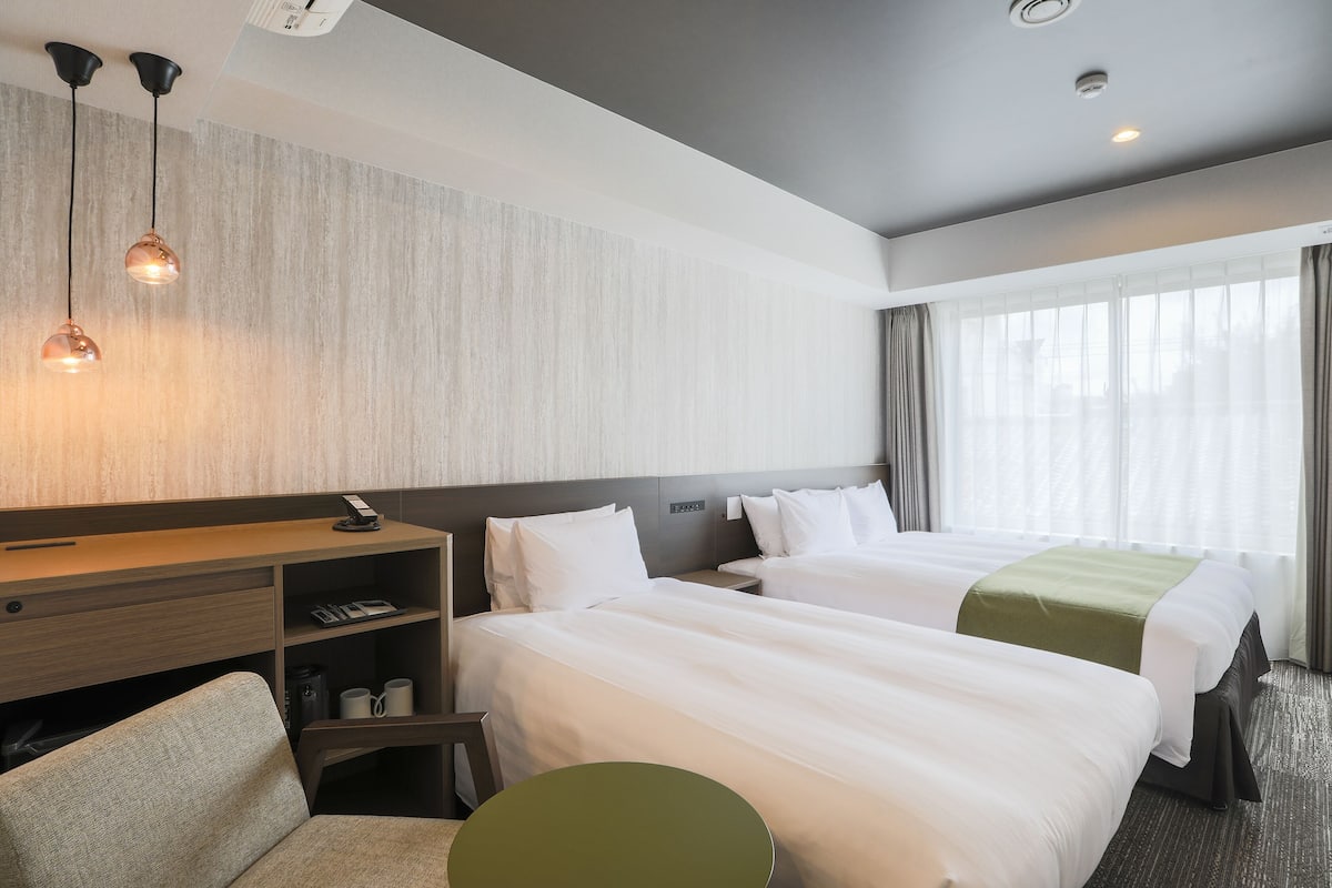 A hotel room with two beds, a desk, a chair, and a small table.