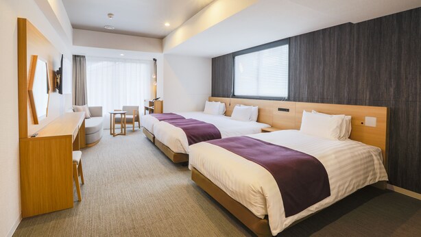 Ein Hotelzimmer mit zwei Betten, einem Schreibtisch, einem Stuhl und einem Fenster mit Jalousien.