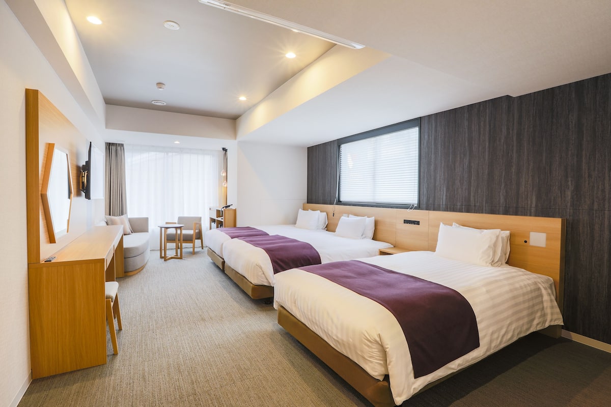 A hotel room with two beds, a desk, a chair, and a window with blinds.