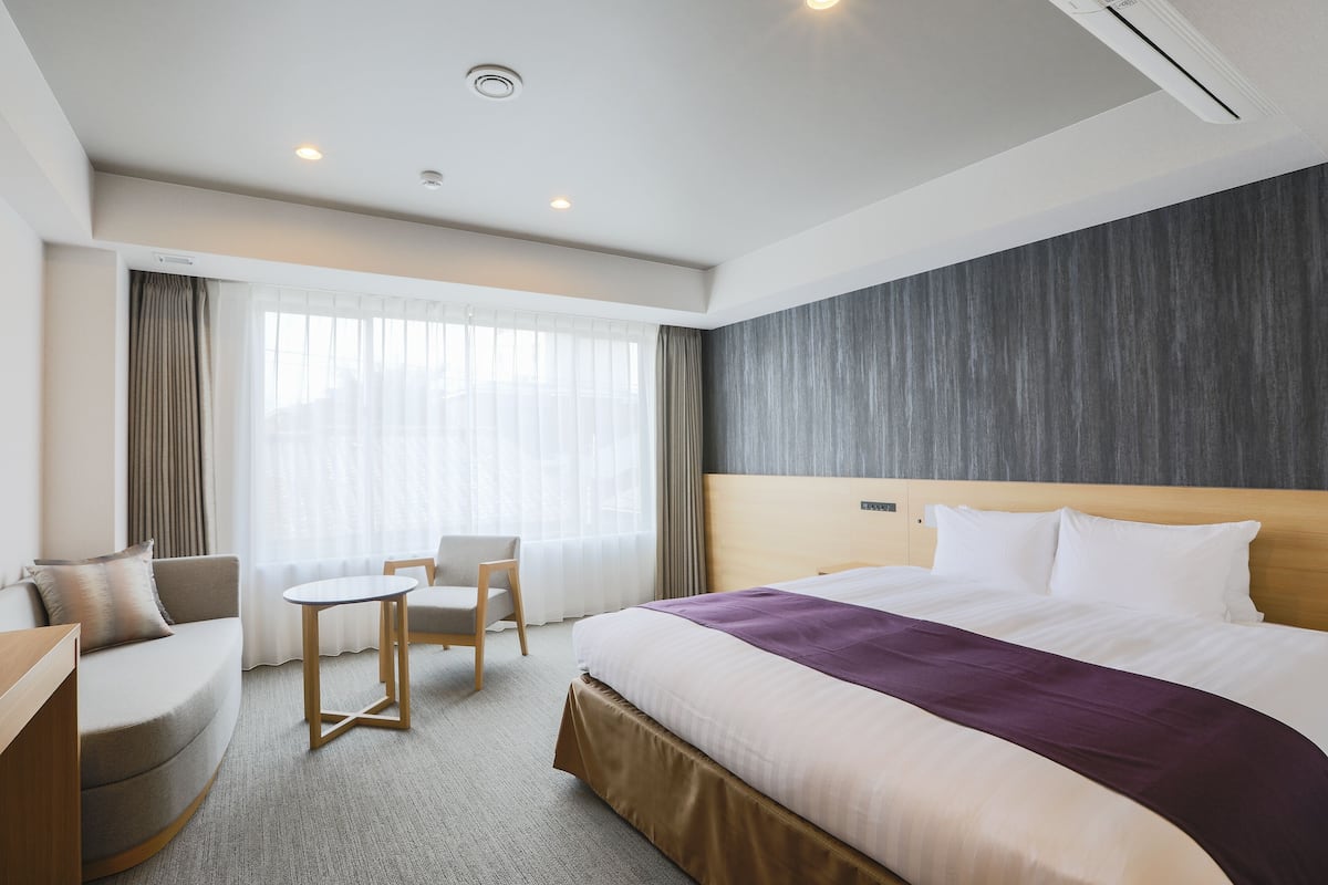 A hotel room with a bed, a sofa, a small table, and a chair.