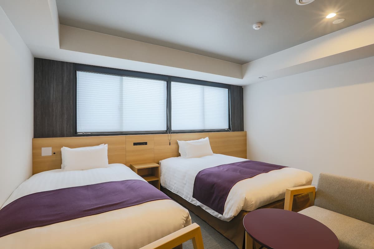 A hotel room with two beds, a small table, and a sofa.