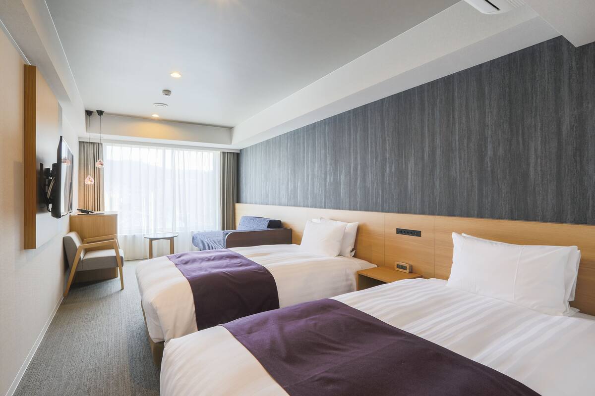 A hotel room with two beds, a desk, a chair, and a television.
