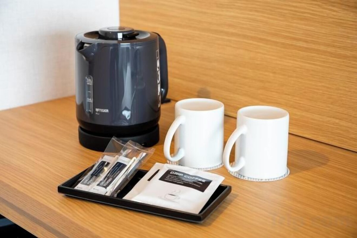 A coffee maker, two white mugs, and a tray with coffee pods and instructions on a wooden surface.