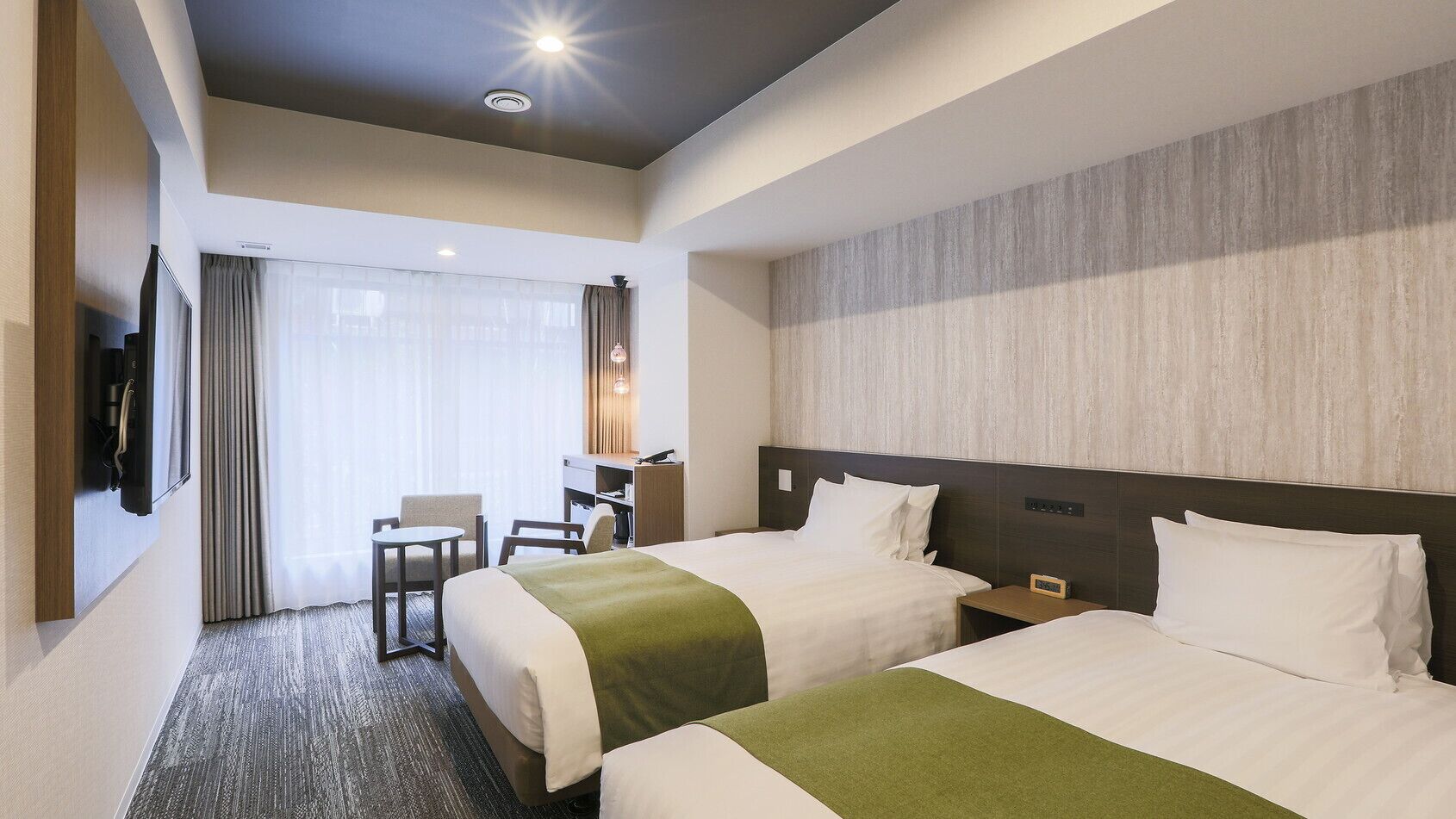 A hotel room with two beds, a desk, a chair, a TV, and a large window with curtains.