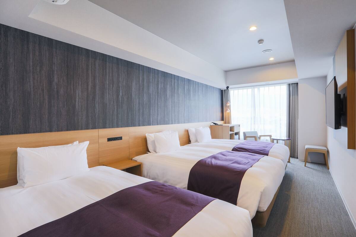 A hotel room with three beds, a wooden headboard, a small table, and a TV on the wall.