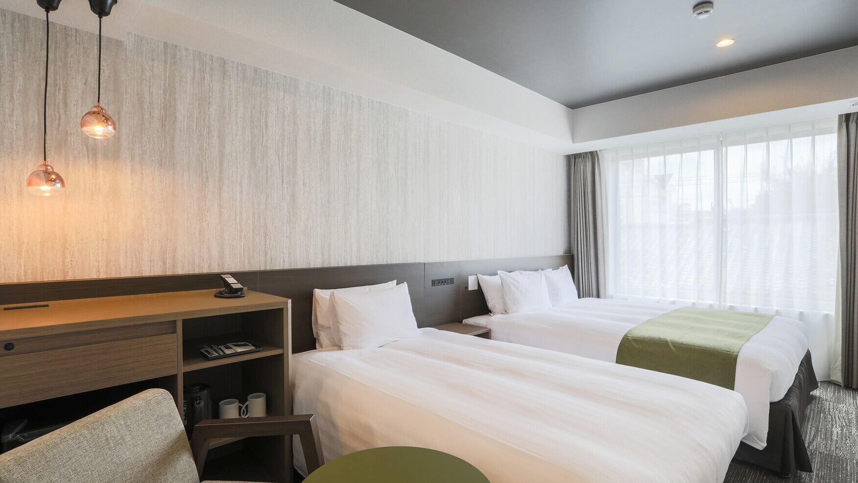 A hotel room with two beds, a desk, a chair, and a large window with curtains.