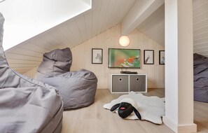 A cozy loft bedroom with a sloped ceiling, a large window, a TV, and artwork on the walls.