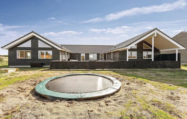 A two-story wooden house with a large deck and a trampoline in the yard.