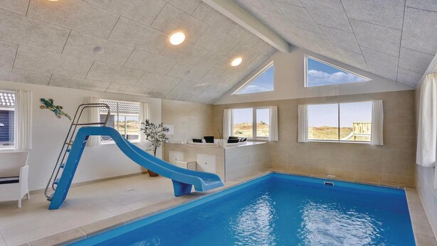 An indoor swimming pool with a blue slide, a sunroof, and a view of the desert landscape. - 8 bedroom awesome home in Thisted (Thisted)