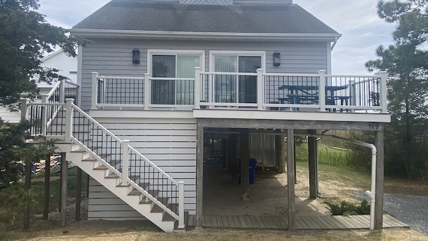 A two-story house with a covered deck and a staircase leading to the upper floor. - Beautiful Broadkill Beach home with a short walk to the beach. (Milton)
