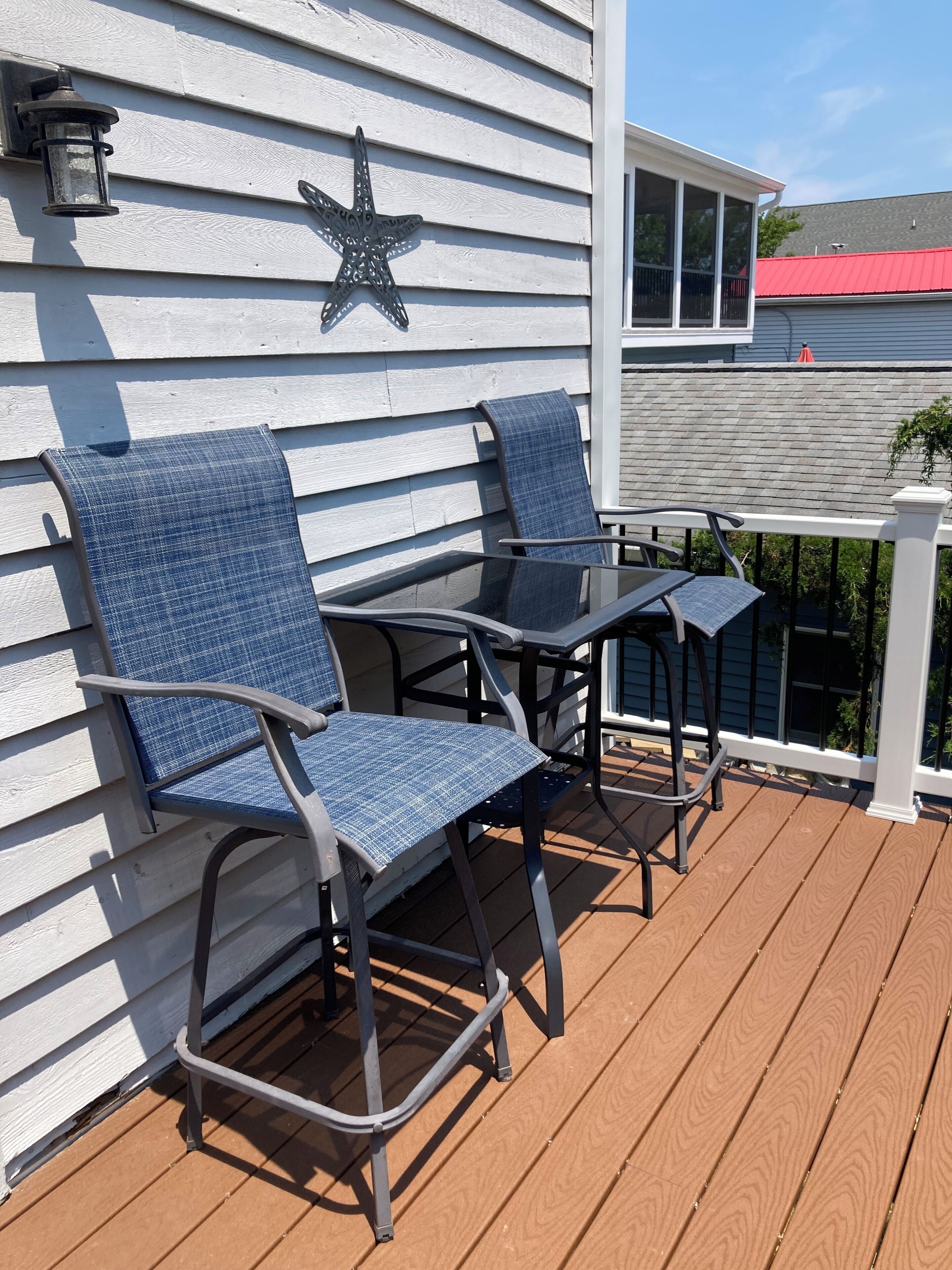A deck with two chairs and a table, a star decoration on the wall, and a red roof in the background.