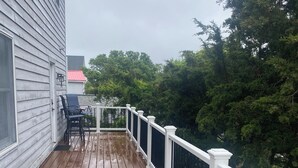 A wooden deck with a white railing, a pair of chairs, and a small table. - Beautiful Broadkill Beach home with a short walk to the beach. (Milton)