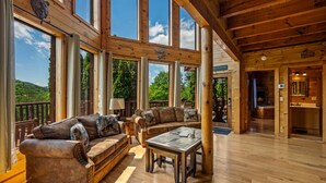 A spacious living area with large windows, a wooden ceiling, and a cozy seating arrangement. - Luxury cabin w/indoor pool, hot tub, view, game rm (Sevierville)