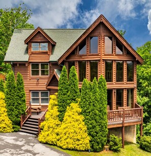 Une grande cabane en rondins à plusieurs étages, dotée d’un balcon et d’un escalier menant à l’entrée.