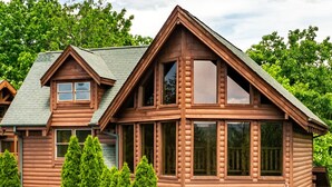 A two-story log cabin with a balcony and a staircase leading to the upper level. - Luxury cabin w/indoor pool, hot tub, view, game rm (Sevierville)