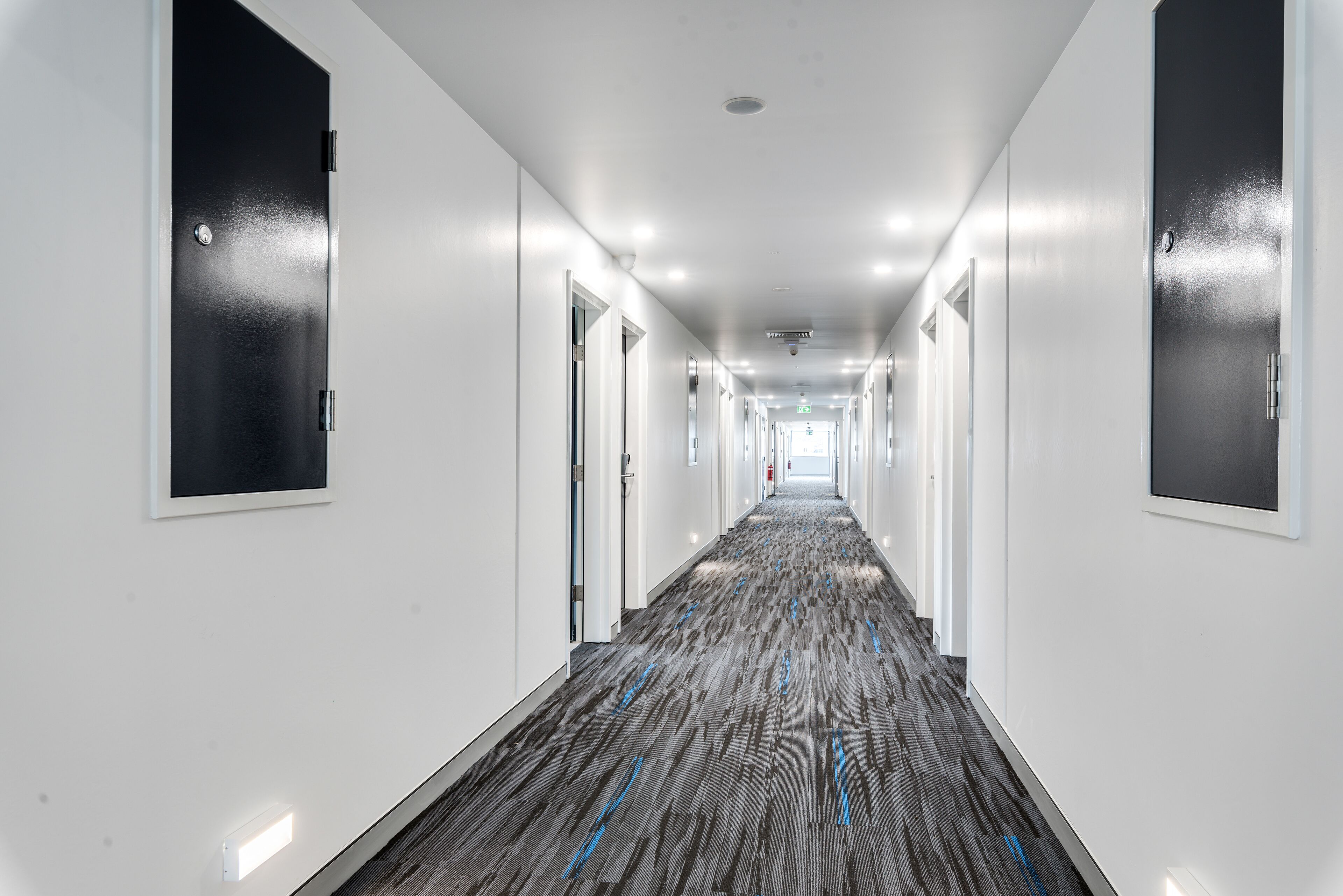 A long, narrow hallway with white walls and a patterned carpet.