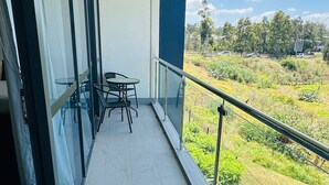 Un balcone con tavolo e sedie, porte vetrate e vista su un paesaggio verde.